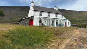 Una casa con base de piedra, un invernadero de cristal y una puerta roja.