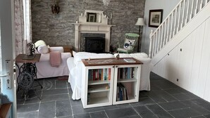 Una habitación acogedora con chimenea, un sofá blanco, una mesita con libros y una escalera.
