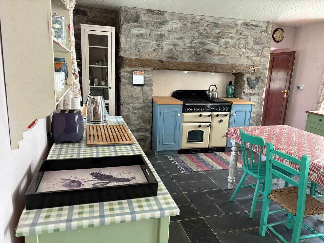 A compact kitchen with a stone wall, a stove, a sink, and a dining area with a table and chairs.