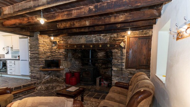 Ein Kamin aus Stein, ein Fernseher, Ledersofas und eine Holzbalkendecke.