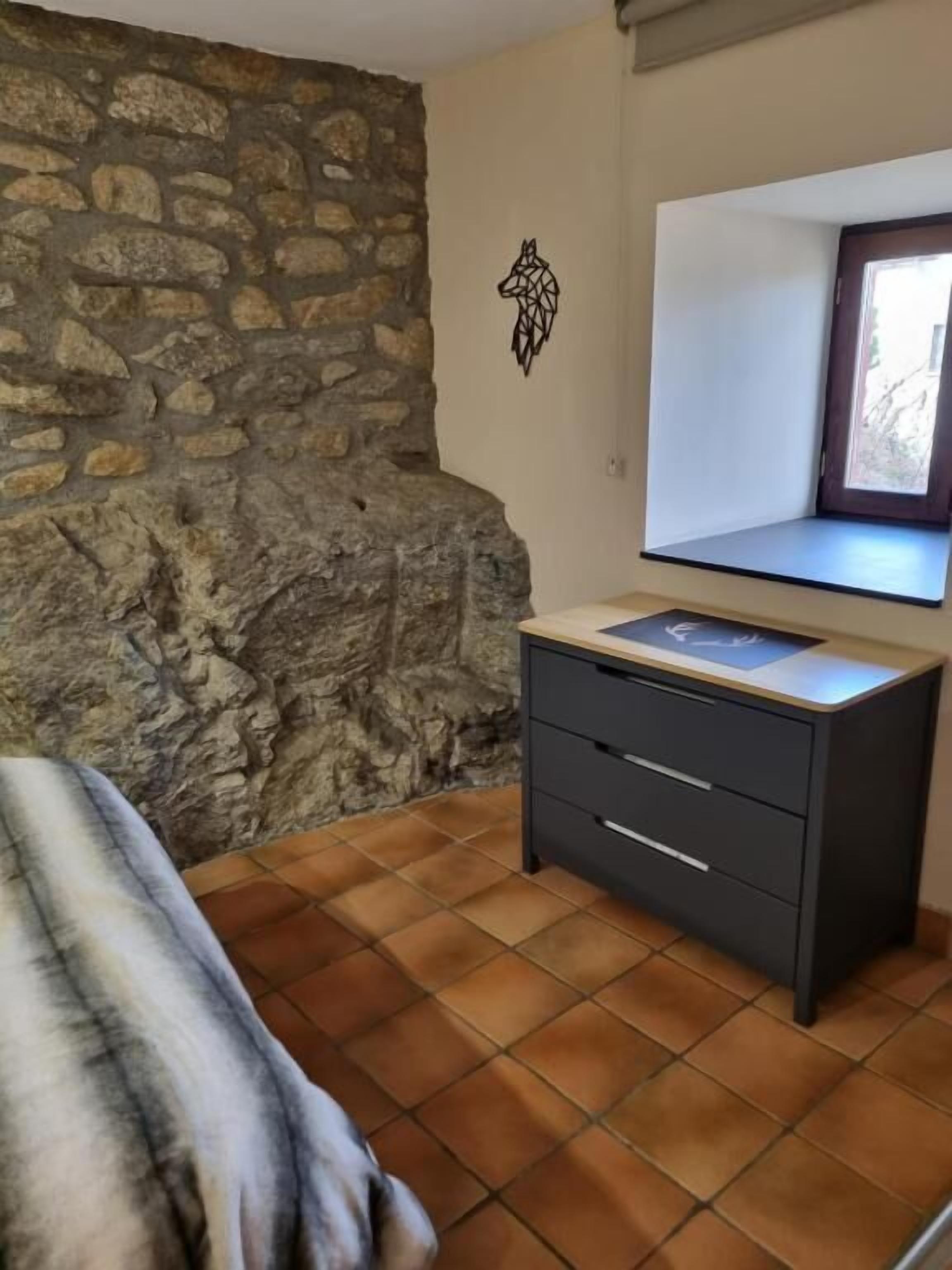 Ein Schlafzimmer mit Steinwand, einem Bett, einem Schminktisch und einem Fenster.
