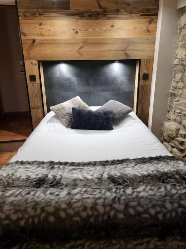 Una cama con cabecera, almohadas y una manta.
