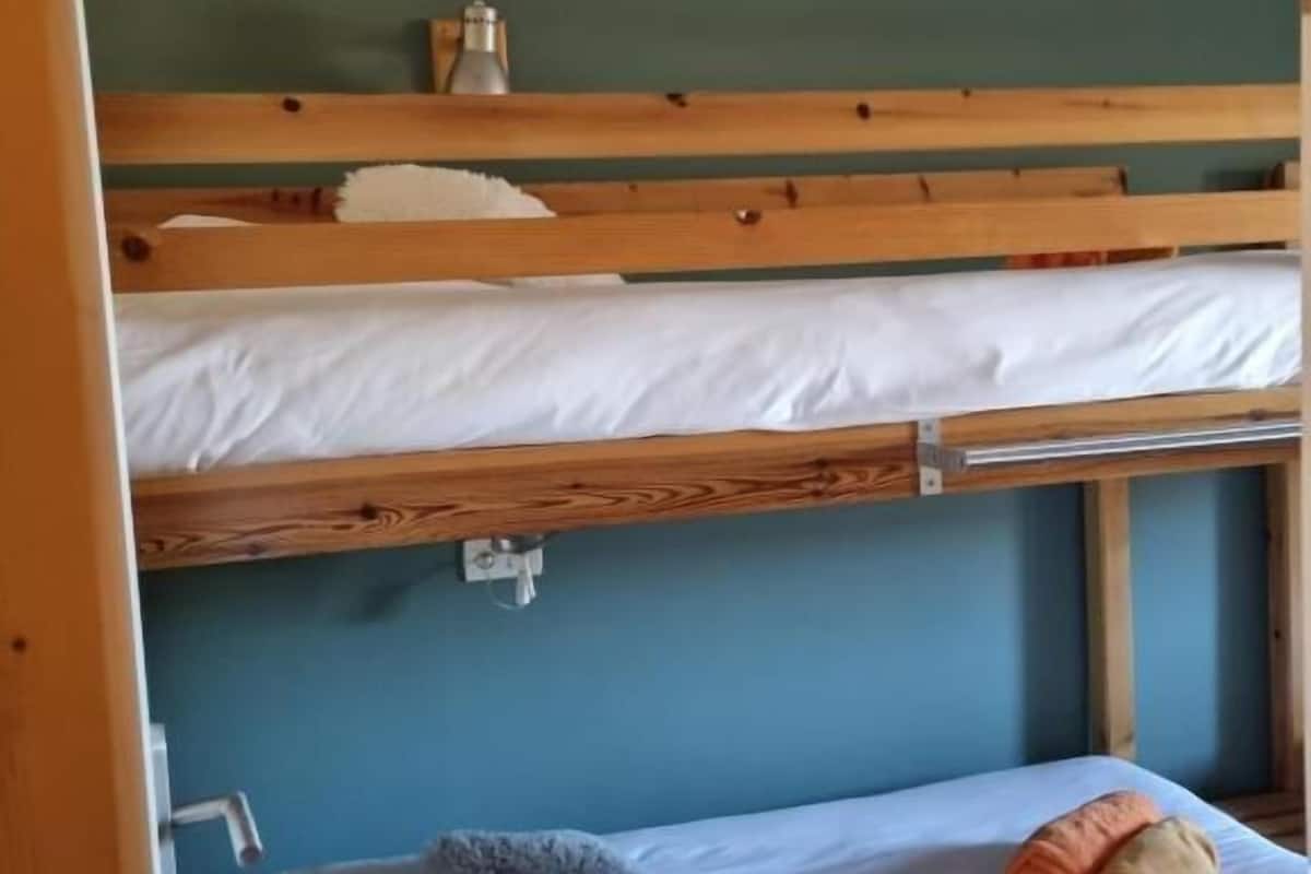 Habitación con literas, pared azul, un estante pequeño con un recipiente y un almohadón blanco en la litera inferior.