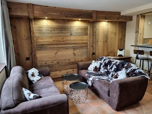 Una sala de estar con un sofá marrón, dos mesas redondas y una pared de madera.