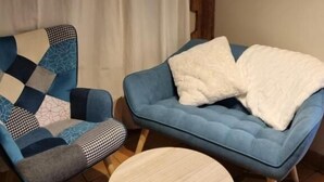 Una habitación con un sofá azul, un sillón estampado y una mesita redonda.