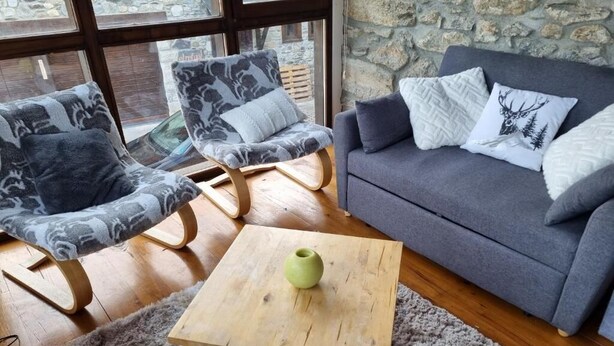 A cozy living room with a grey sofa, patterned armchairs, a wooden coffee table, and a stone wall. - Orri de Planès (Planès)
