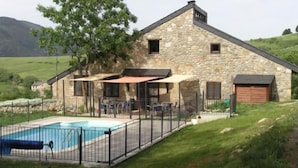 A stone building with a pool, outdoor seating, and a fenced area. - Orri de Planès (Planès)