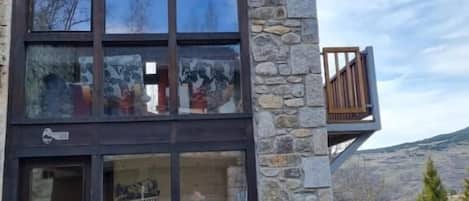 A stone building with a glass entrance, a wooden bench outside, and a mountain view.