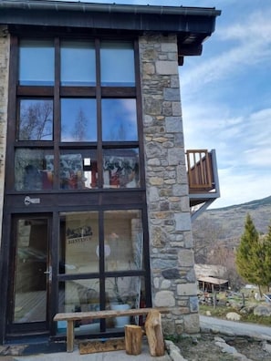 Un edificio de piedra con entrada de vidrio, un banco de madera en el exterior y vista a la montaña.