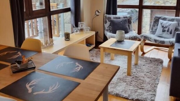 Una habitación acogedora con una mesa de madera, sillas, un sofá y ventanas amplias.
