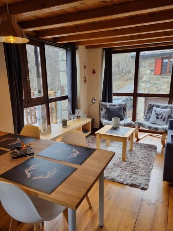 A cozy room with a wooden table, chairs, a sofa, and large windows.