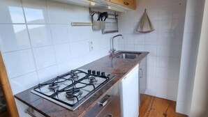 A kitchen with wooden cabinets, a gas stove, a sink, and a white tiled backsplash. - Orri de Planès (Planès)