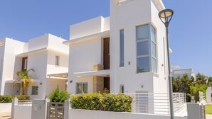 A modern multi-story building with balconies, a gated entrance, and a clear blue sky. - Milos lifestyle villas H9- 4 bedroom villa with private pool (Paralimni)