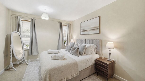 Een slaapkamer met een bed, nachtkastje, lamp, spiegel en een schilderij aan de muur.