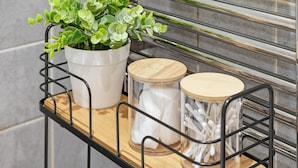 Een metalen plank met een potplant, een glazen pot met een houten deksel en een bakje met witte wattenstaafjes.