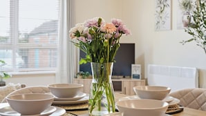Een eettafel met kommen en borden, een vaas met bloemen, en een televisie op de achtergrond.
