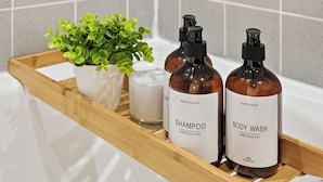 Een badkamerplankje met een plant in pot, een kaars en twee flessen shampoo en douchegel.