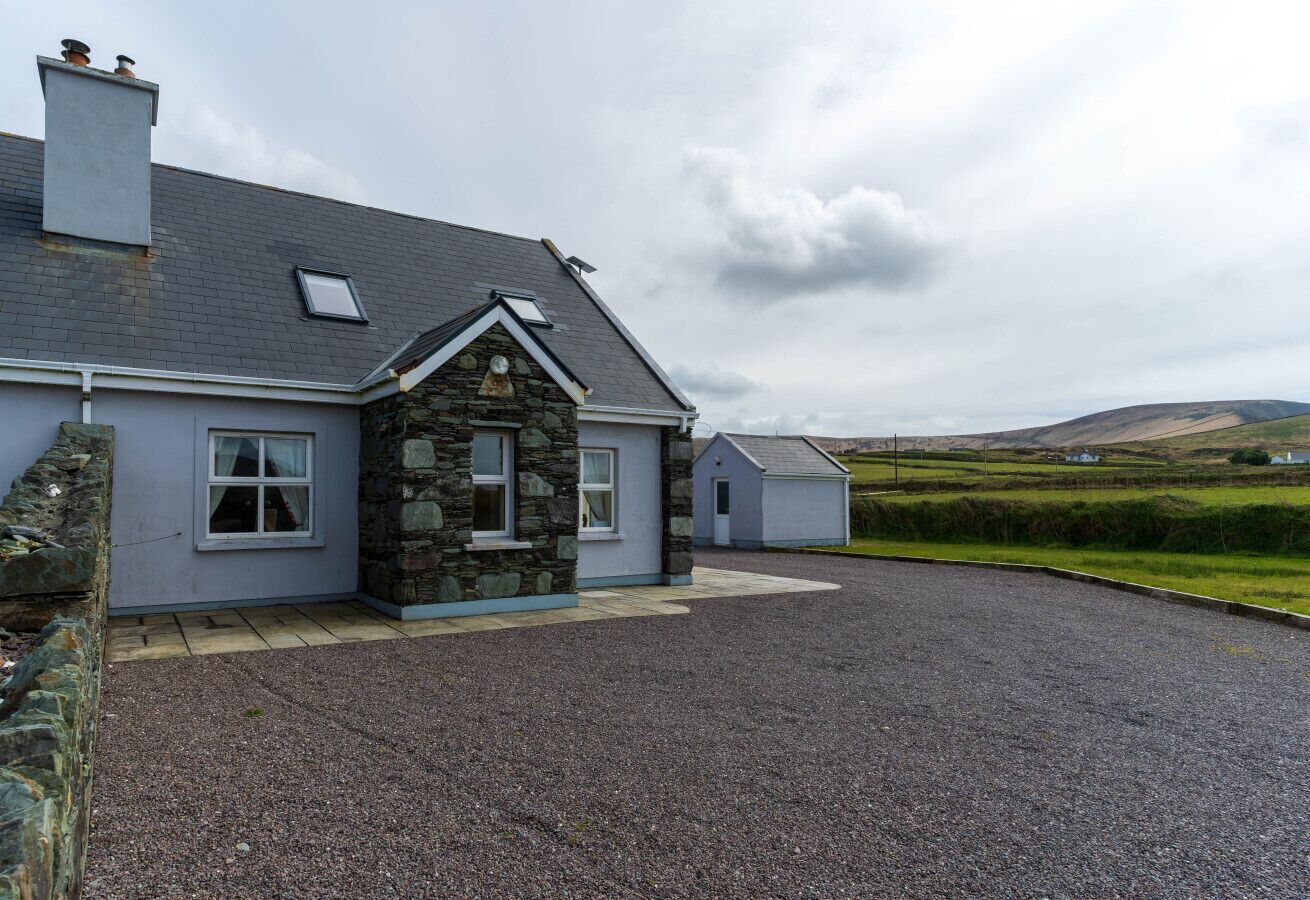 Une maison avec une façade en pierre, un toit gris et une allée gravillonnée.