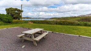 Une table de pique-nique se trouve dans un espace herbeux, offrant une vue sur un lac et des collines en arrière-plan.