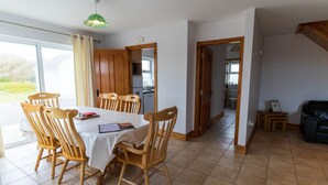 Un coin repas avec une table et des chaises, une cuisine en arrière-plan et une vue à travers une porte vitrée.