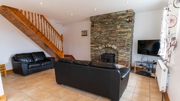 Un salon avec une cheminée en pierre, un canapé noir, un escalier en bois et un téléviseur à écran plat.