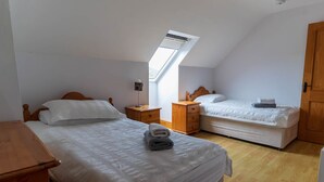Une chambre avec deux lits, des meubles en bois, une lucarne et une porte en bois.