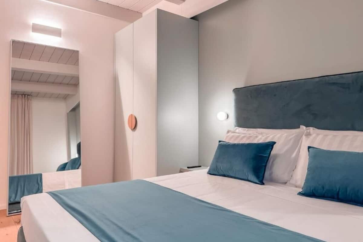 A modern hotel room with a large bed, a headboard, a bedside table, and a mirror.