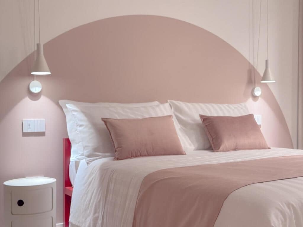 Un dormitorio con cama, mesitas de noche e iluminación en la pared.