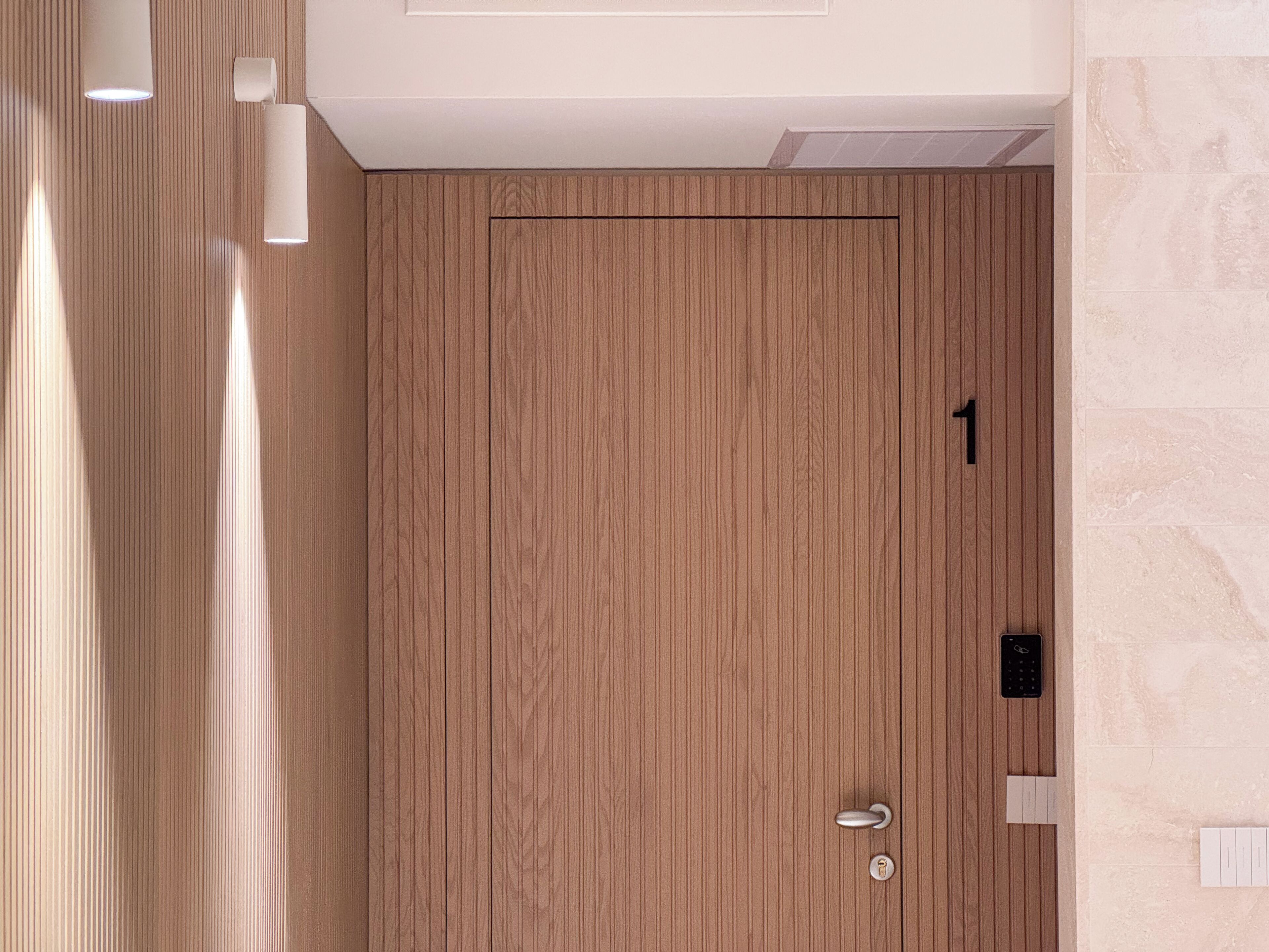 Una puerta de madera con cerradura electrónica, una pequeña ventana y una lámpara fijada a la pared.