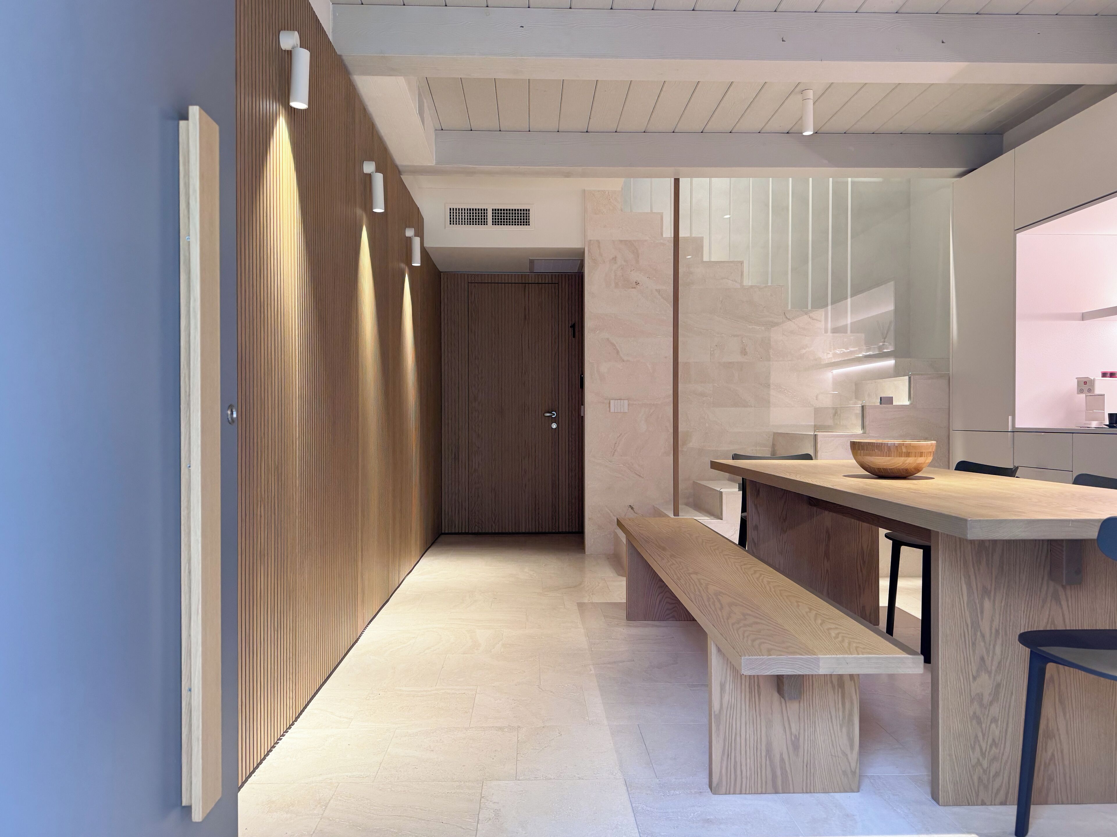 Une cuisine moderne avec un banc en bois, un grand îlot central doté d’un évier et une vue sur le couloir.