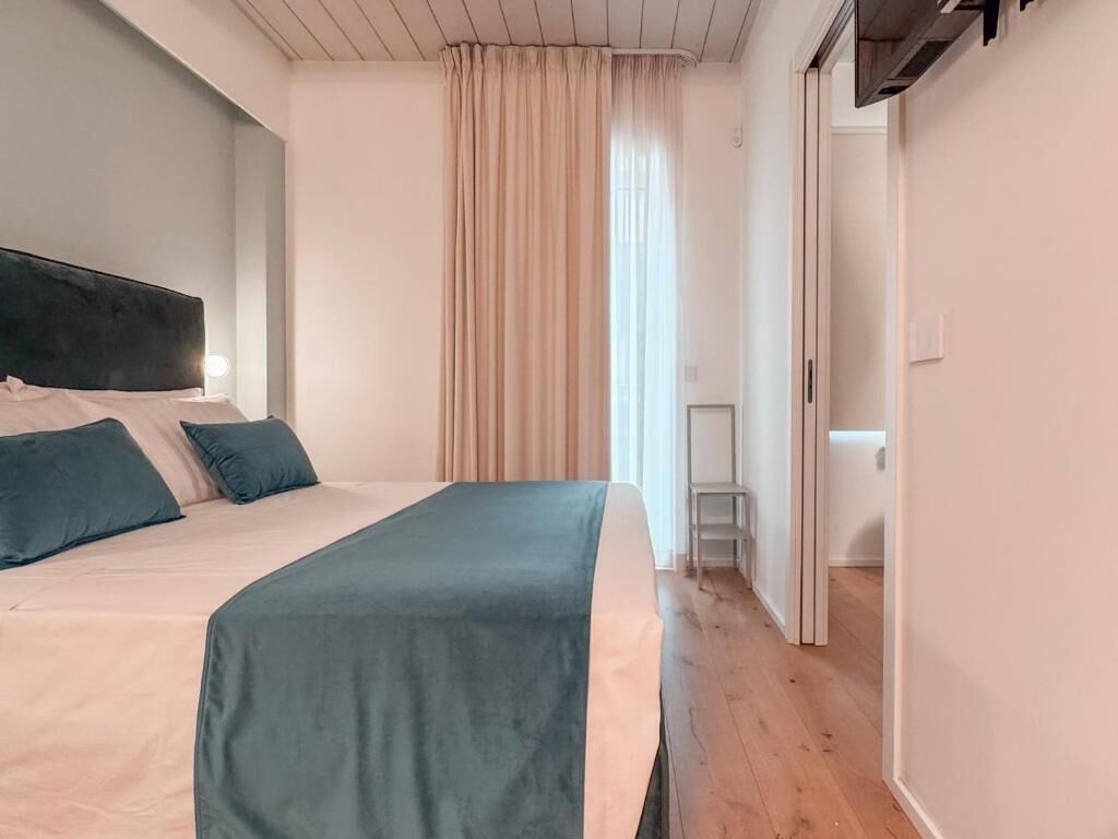 Une chambre à coucher avec un lit, une tête de lit, une fenêtre avec des rideaux et un plancher en bois.
