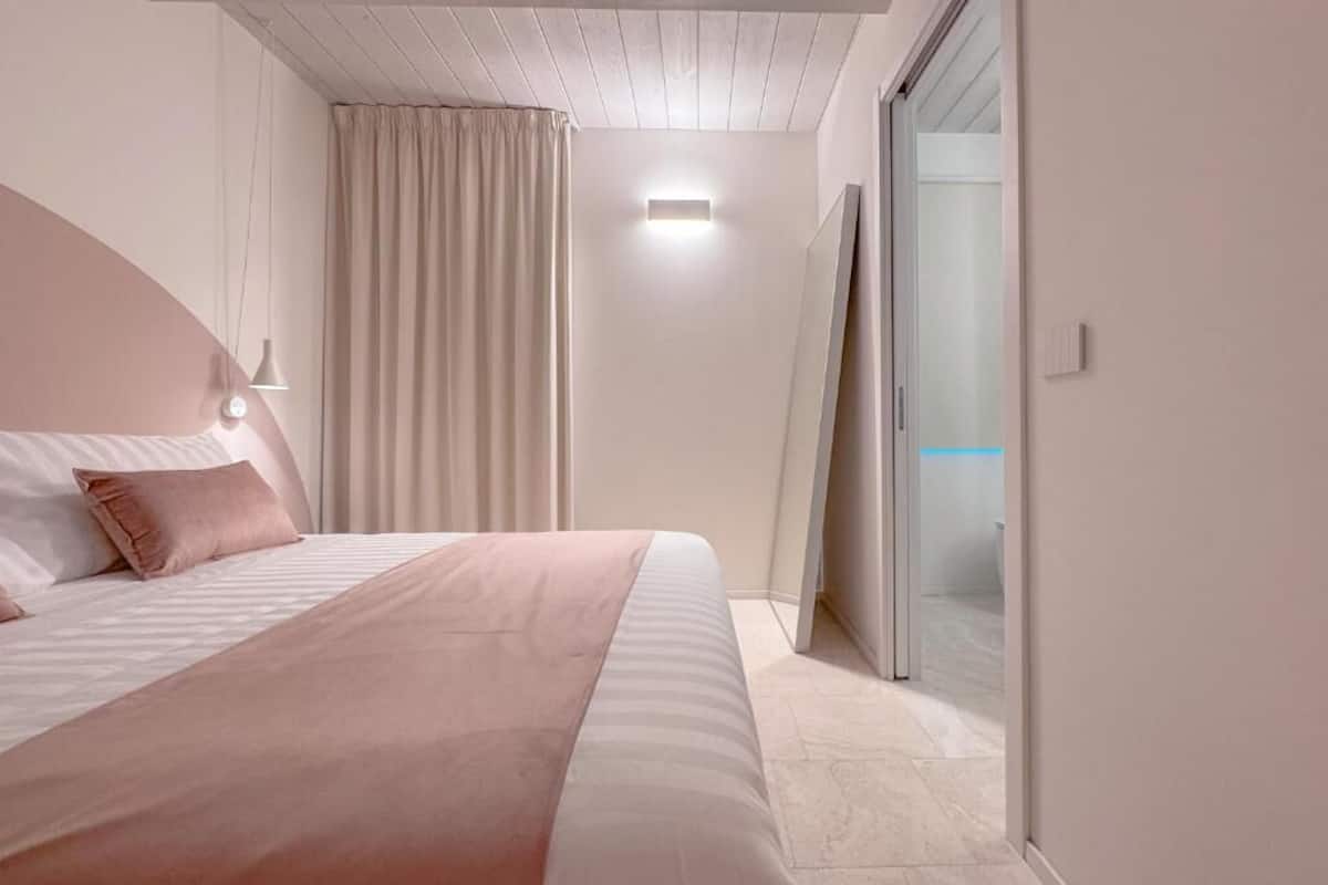 A bedroom with a bed, a bedside lamp, a window with curtains, and a sliding door leading to a balcony.