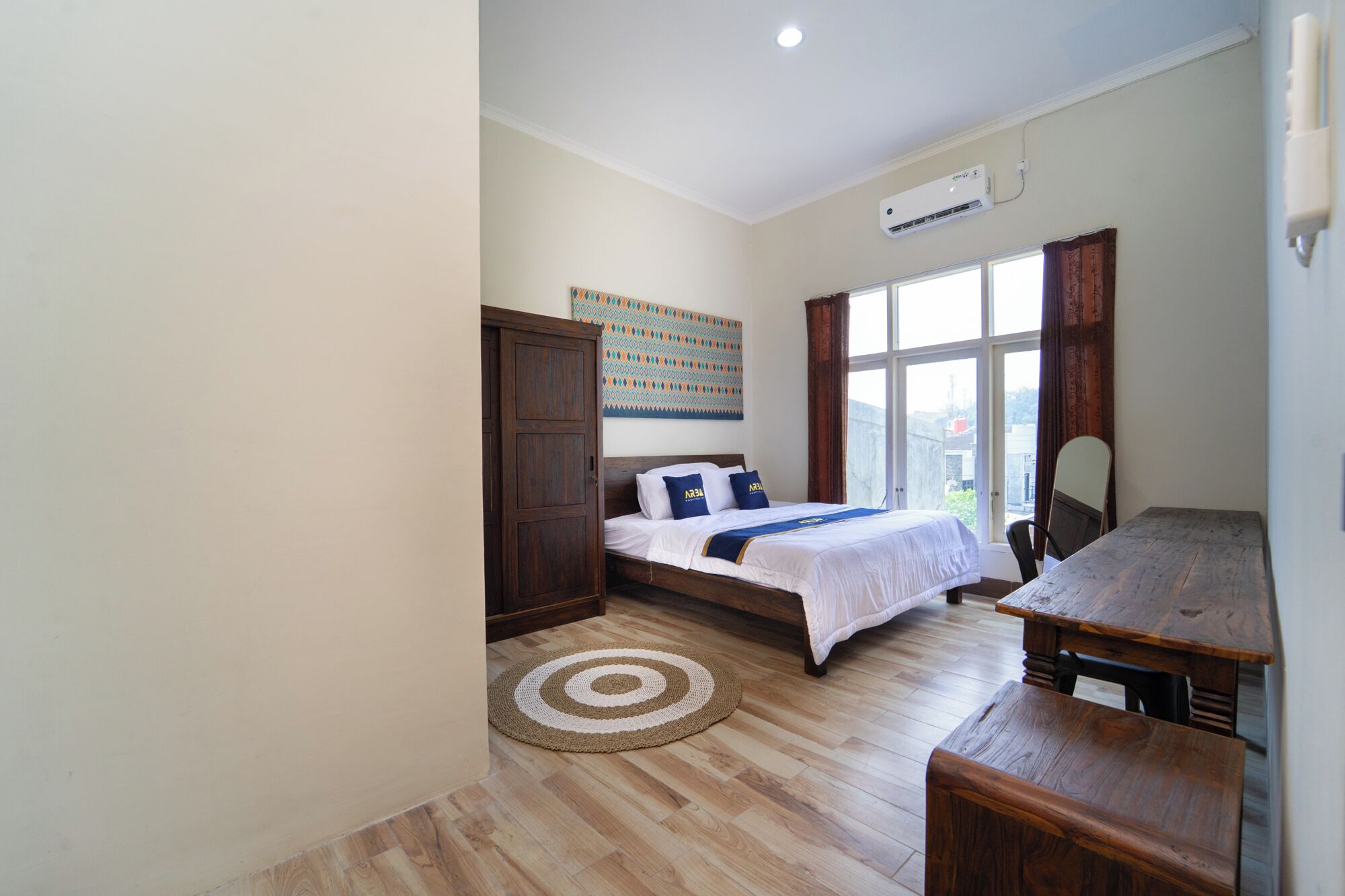 Quarto com cama, escrivaninha, cadeira, janela e ar-condicionado.
