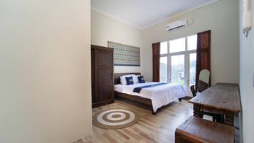A bedroom with a bed, a desk, a chair, a window, and an air conditioning unit.