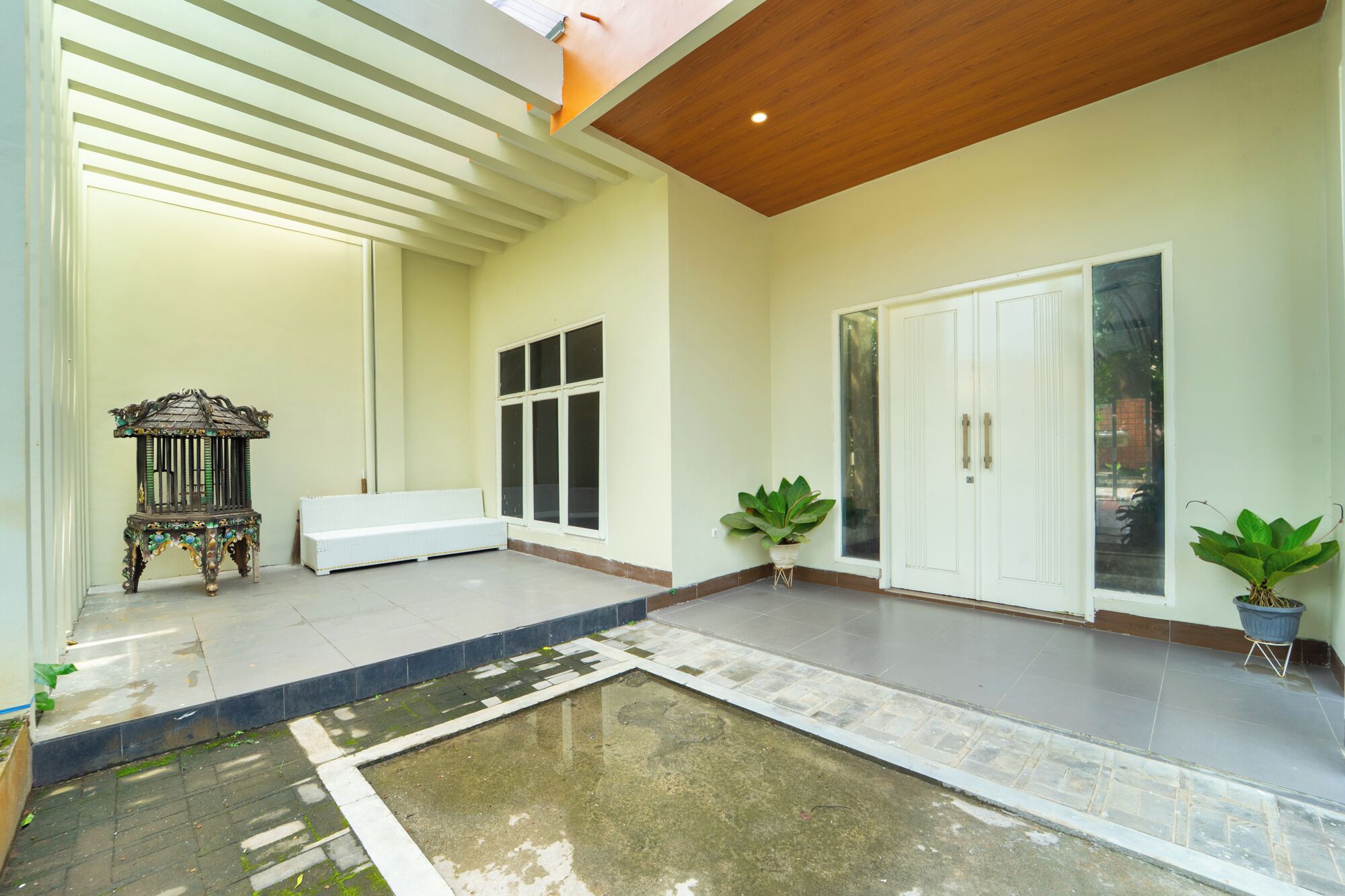 Un patio espacioso con un banco blanco, una jaula decorativa y plantas en macetas.