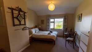 Ein Schlafzimmer mit einem Bett, einem Sessel, einem Schreibtisch, einer Heizung, einem Fenster mit Vorhängen und einer Pendelleuchte.