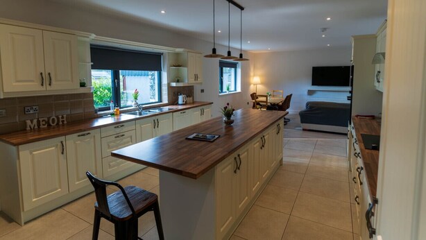 Una cocina moderna con armarios blancos, una isla de madera y un comedor con una silla.