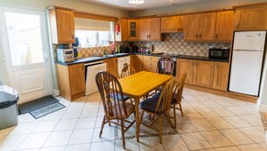 A kitchen with wooden cabinets, a dining table with chairs, a microwave, and a refrigerator. - Riverview House Ireland Stay – Scenic Riverside Holiday Home in County Kerry (Cahersiveen)