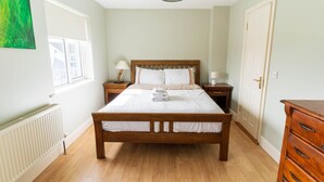 A bedroom with a wooden bed, white bedding, a nightstand with a lamp, a dresser, and a radiator. - Riverview House Ireland Stay – Scenic Riverside Holiday Home in County Kerry (Cahersiveen)