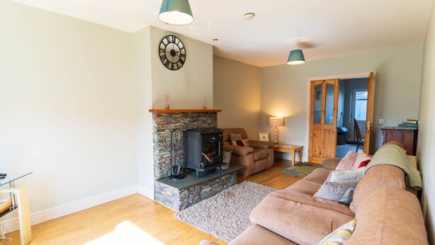 A cozy living room with a stone fireplace, a large clock, and a sofa. - Riverview House Ireland Stay – Scenic Riverside Holiday Home in County Kerry (Cahersiveen)