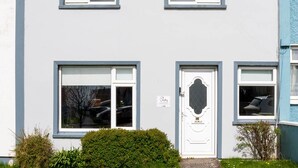 A two-story residential building with a white facade, a central door with a decorative glass panel, and a small garden area with grass and flowers. - Riverview House Ireland Stay – Scenic Riverside Holiday Home in County Kerry (Cahersiveen)