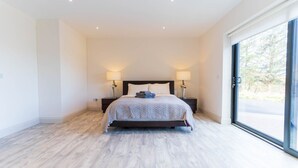 Una camera da letto moderna con un letto grande, due comodini con lampade e una porta vetrata scorrevole che dà su un balcone.