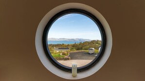 Una finestra rotonda con vista su un paesaggio che include un edificio, un camper e un corpo d'acqua.