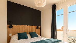 Une chambre à coucher moderne avec un lit, une tête de lit en bois, un luminaire suspendu et une vue sur l’extérieur.