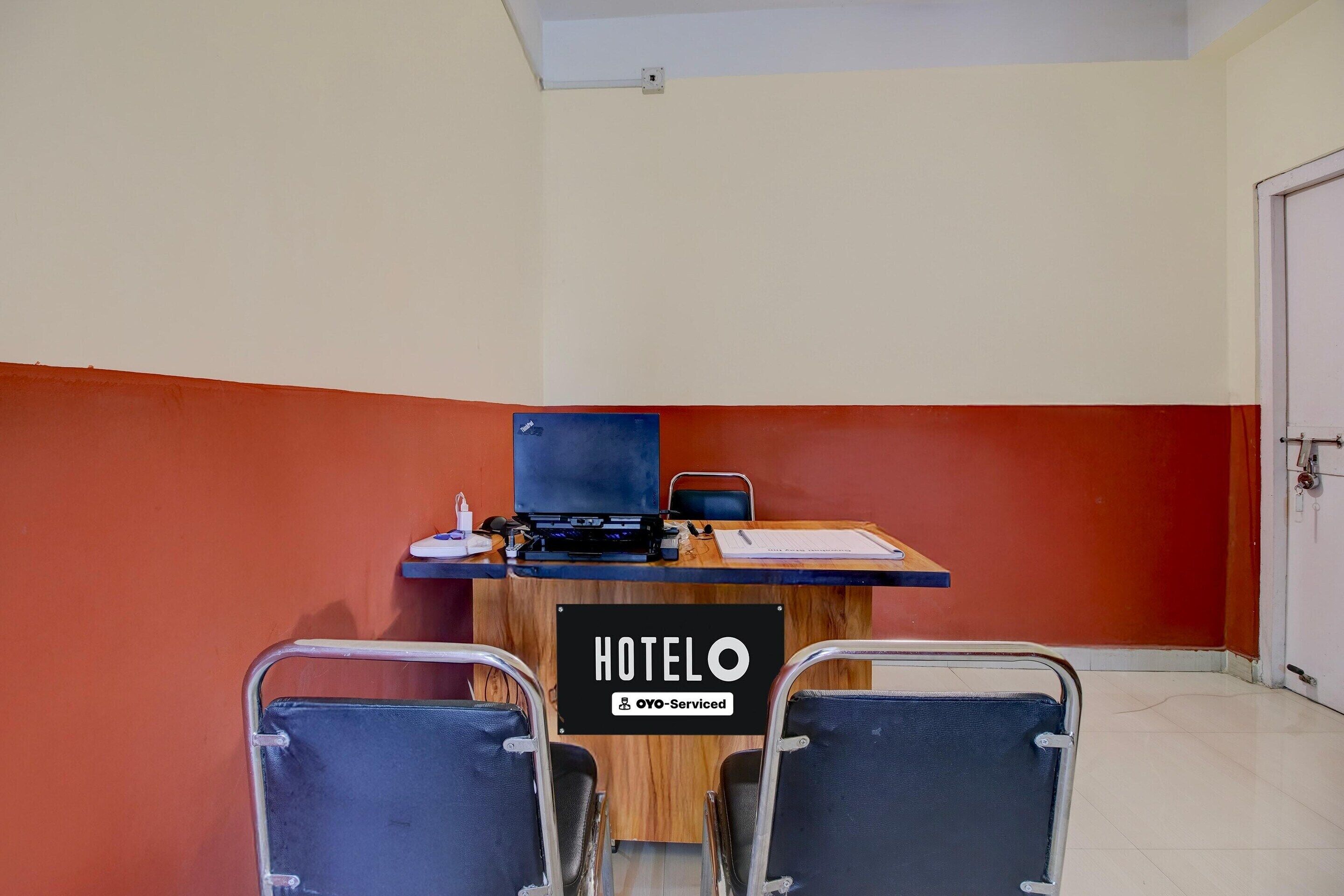Habitación de hotel con escritorio, dos sillas, una computadora portátil y un letrero que dice 'HOTELO OYO-Serviced'.