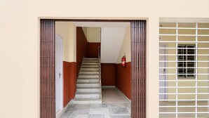 A hallway with a staircase leading to a door, a fire extinguisher on the wall, and a window with a metal grid. - Classic Guwahati Stay Inn (Guwahati)