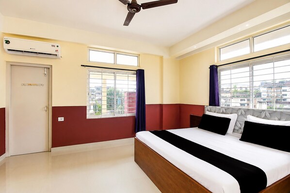 A hotel room with a bed, windows, an air conditioning unit, and a door.