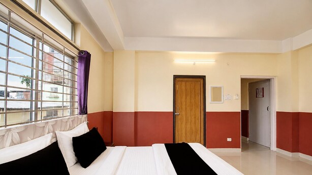 A hotel room with a large bed, a window with blinds, a door, and a hallway. - Classic Guwahati Stay Inn (Guwahati)