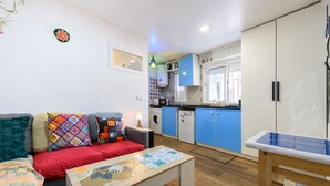 A compact living space with a sofa, a coffee table, a dining table, a kitchen area with blue cabinets, and a washing machine. - (MDP80314) 1 bedroom apartment in the center of Madrid (Madrid)