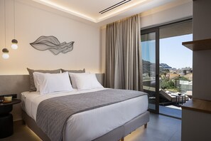 A modern hotel room with a large bed, a view of the city, and a balcony with a table and chairs. - Maple Villa 2 Superior Sea View Villa, Walking Distance From Plakias Beach (Agios Vasileios)